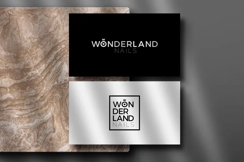 Tarjetas negra y plateada con el logo de Wonderland Nails sobre piedra